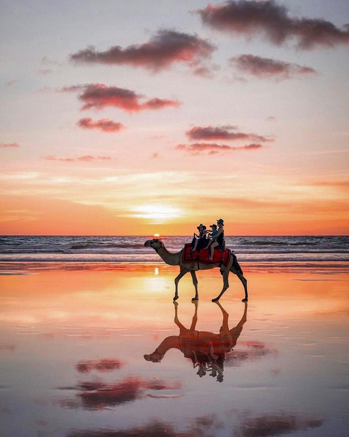 Camel riders reflected on wet sand at Cable Beach at sunset